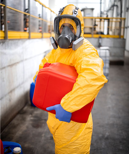 Persona con traje amarillo de protección química y mascarilla con filtros, sosteniendo un bidón rojo